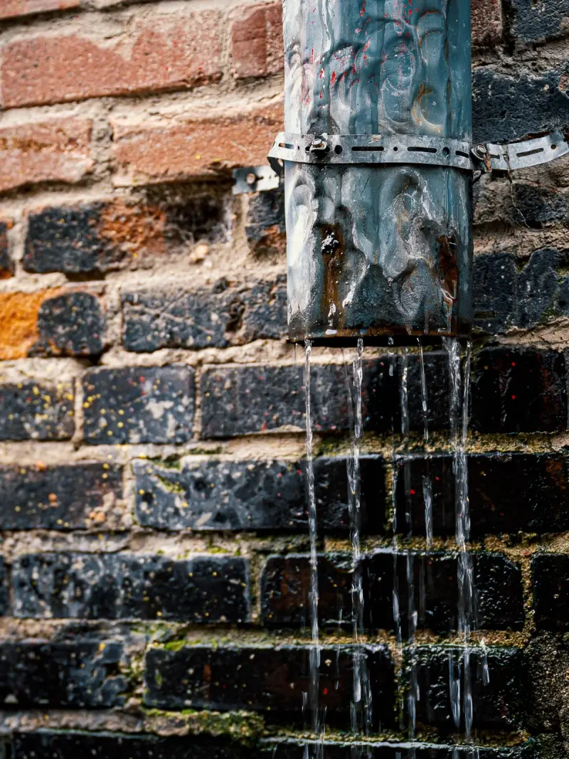 Water stroomt uit een kapotte pijp over een bakstenen muur